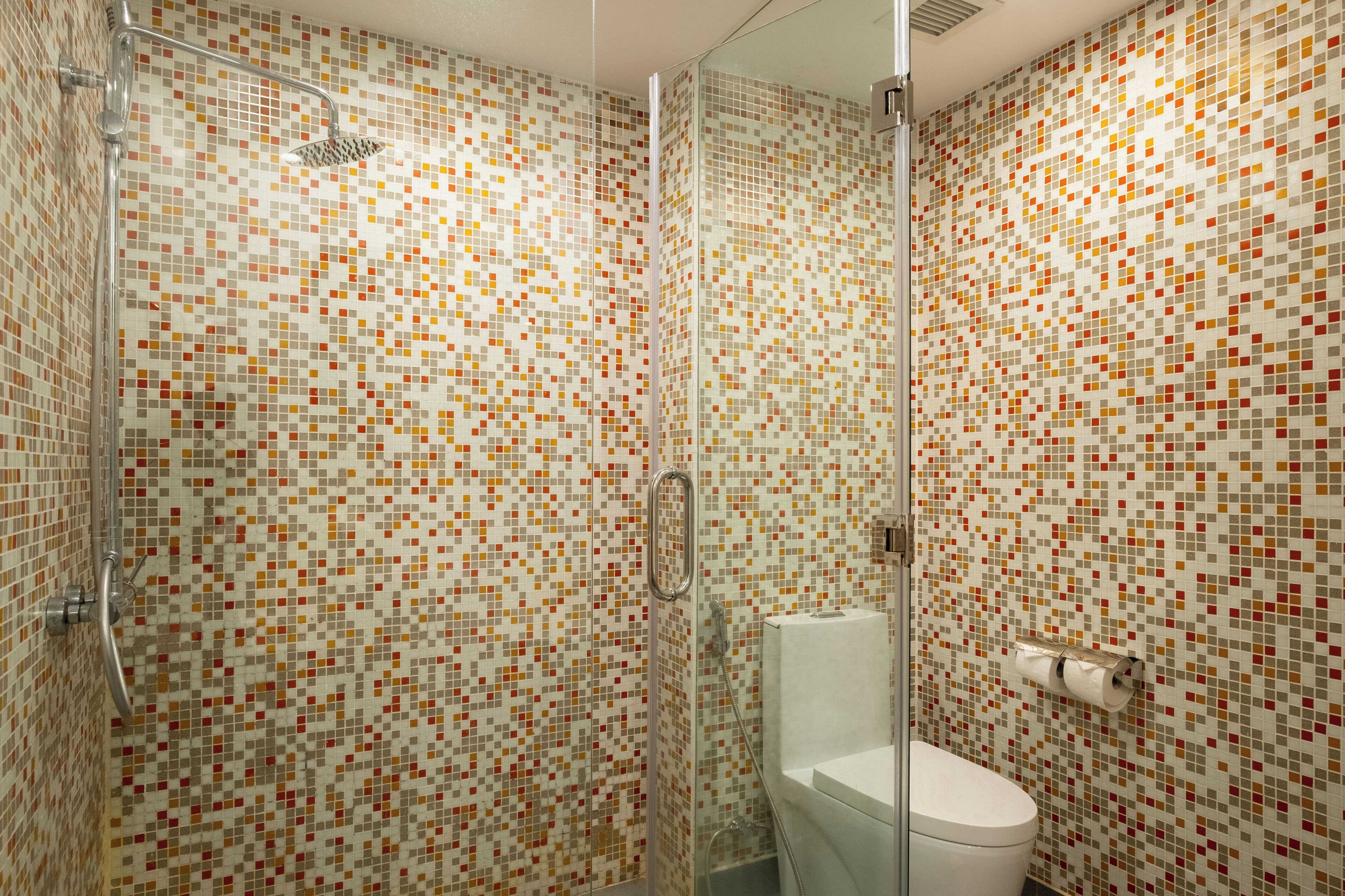 A bathroom with mosaic tile walls, a glass shower enclosure, and a toilet.