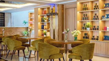 A modern hotel lobby with a wooden reception desk, green upholstered chairs, and shelves stocked with products.
