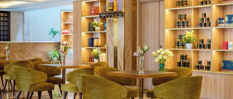 A modern hotel lobby with a wooden reception desk, green upholstered chairs, and shelves stocked with products.