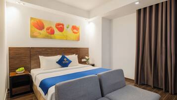 A hotel room with a bed, a nightstand, a blue throw blanket, a wooden headboard, and a painting of flowers on the wall.