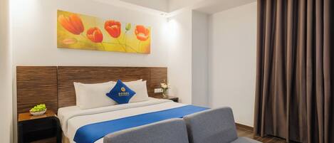 A hotel room with a bed, a nightstand, a blue throw blanket, a wooden headboard, and a painting of flowers on the wall.