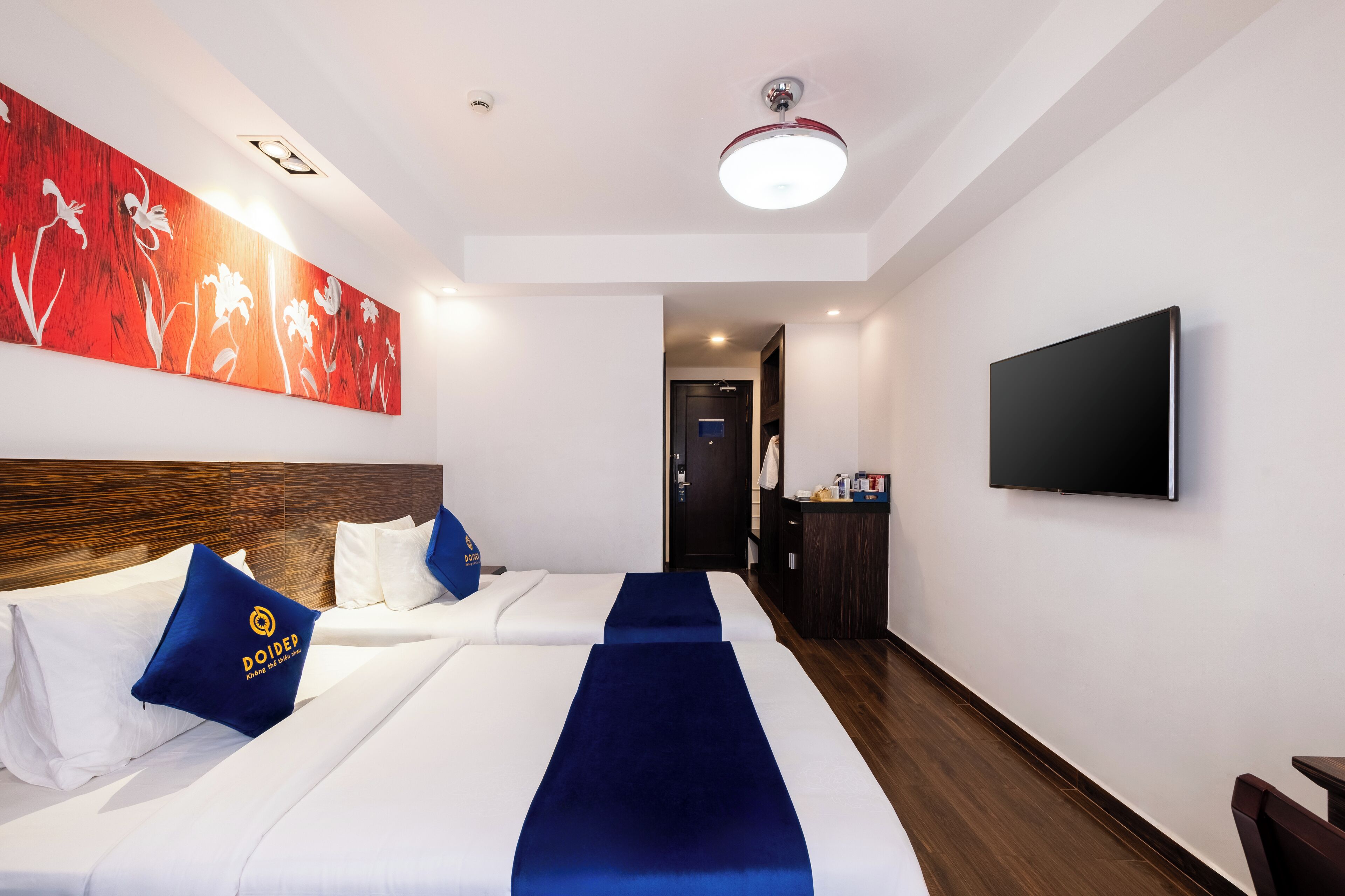 A hotel room with two beds, a large artwork on the wall, a flat-screen TV, and a wooden floor.