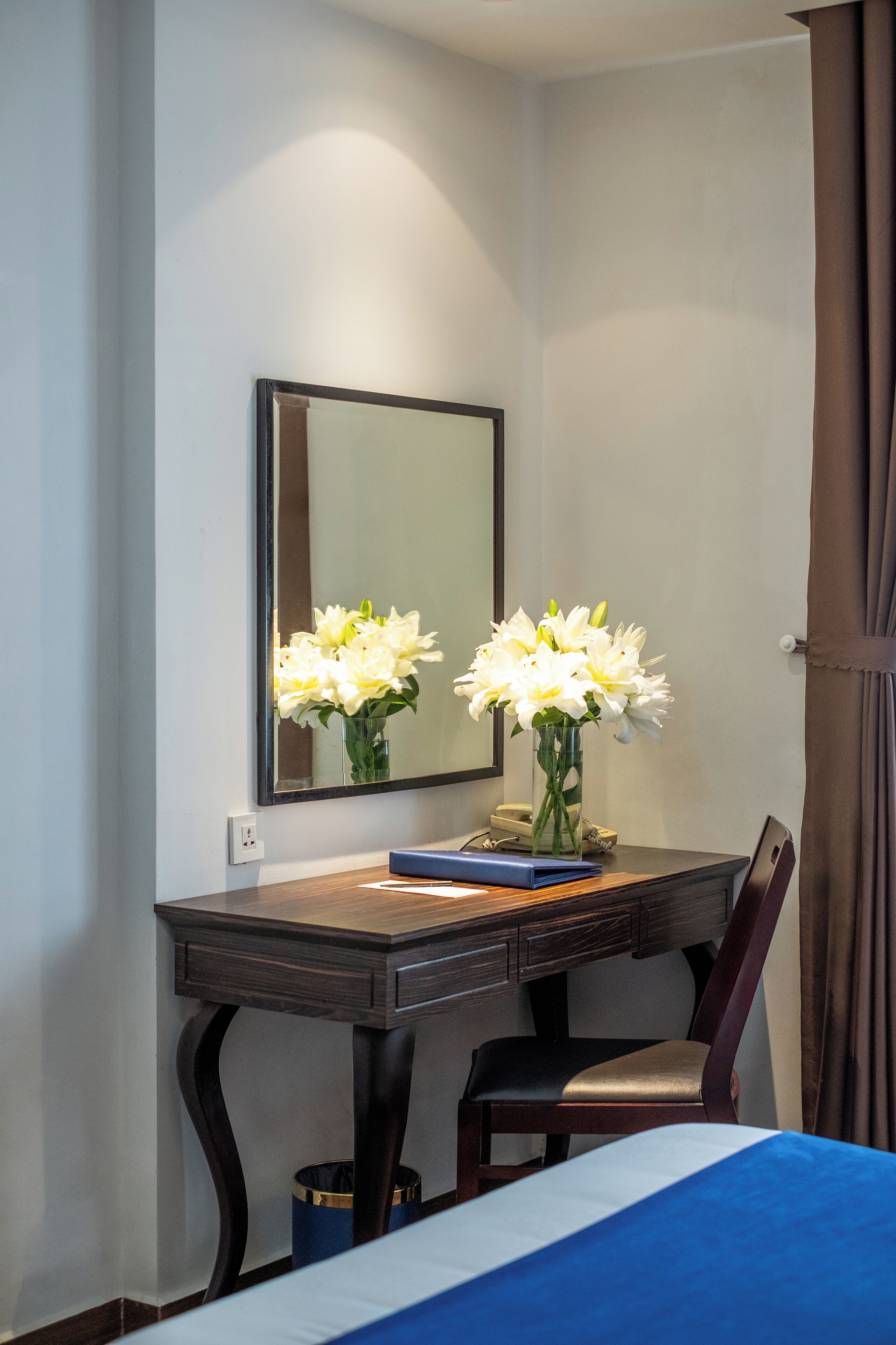 Een hotelkamer met een bed, een bureau met stoel, een spiegel en een vaas met bloemen.