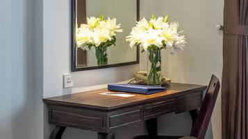 Een hotelkamer met een bed, een bureau met stoel, een spiegel en een vaas met bloemen.
