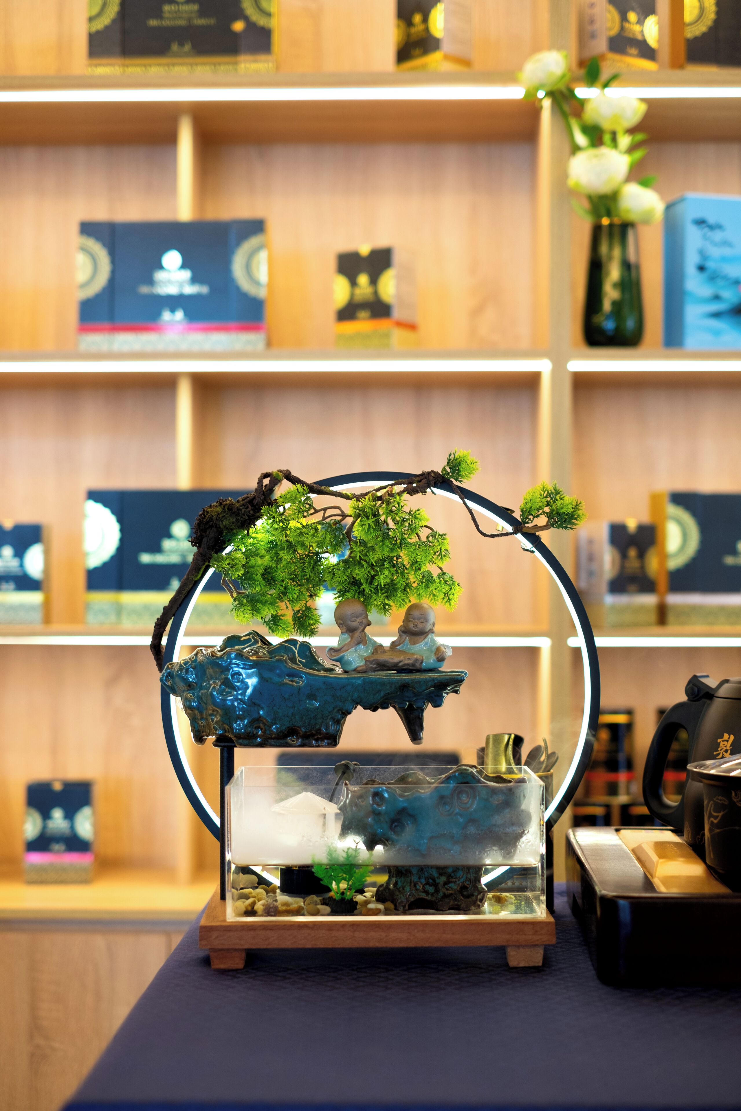 Un jardin d’intérieur décoratif comprenant un bonsaï, un petit bateau et une statue de Bouddha.