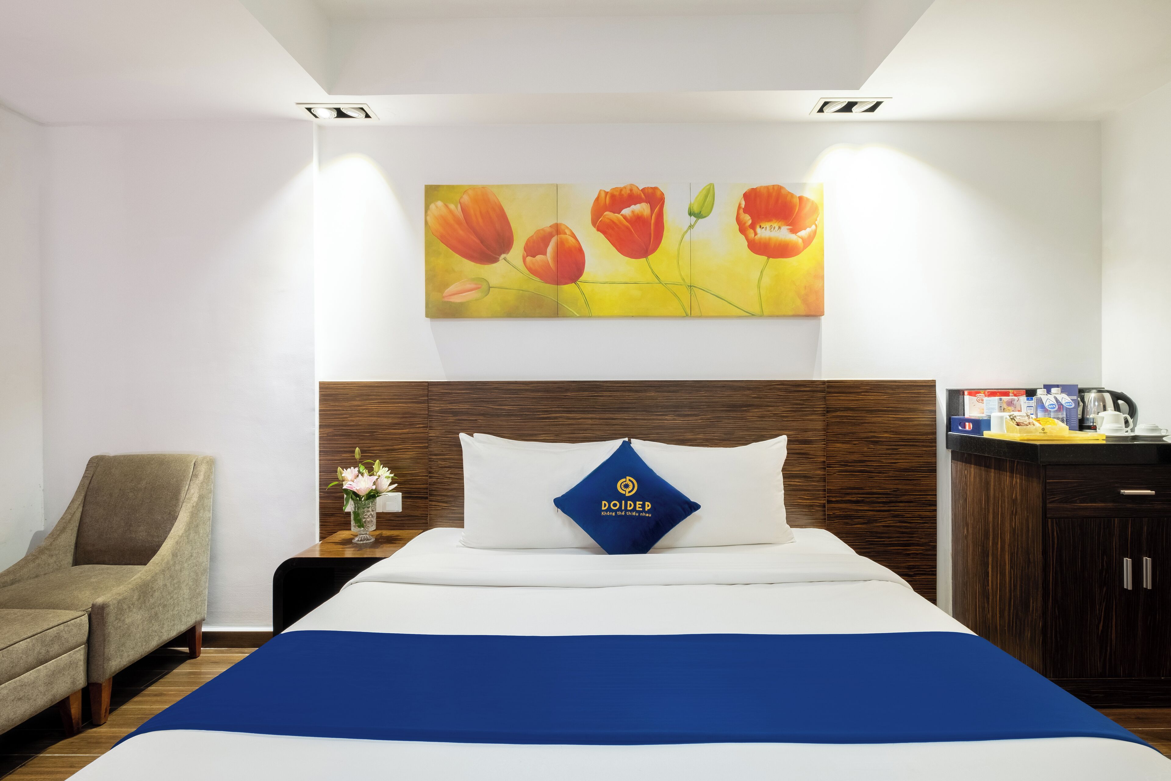Une chambre d’hôtel avec un lit, une chaise, une table de chevet et un tableau représentant des fleurs accroché au mur.