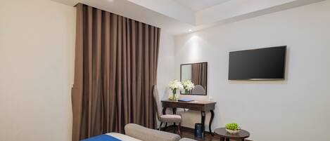 Habitación de hotel con cama, escritorio, silla, una pequeña mesa con planta y televisor de pantalla plana montado en la pared.