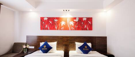 A hotel room with two beds, a wooden headboard, a red floral artwork, and a small table with a vase.