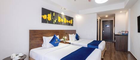 A hotel room with two beds, a small table with a tea set, a painting on the wall, and a ceiling fan.
