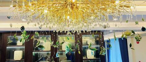 Um candelabro com várias lâmpadas e plantas penduradas em um quarto com prateleiras de madeira exibindo diversos objetos.