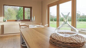 Een moderne keuken met een houten tafel, een glazen vaas en uitzicht op de tuin door grote ramen.