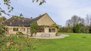 Een stenen huis met een schuin dak, een overdekte veranda en een verzorgd gazon.
