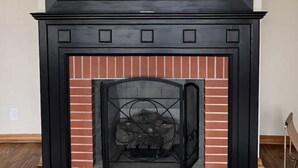 Ein Kamin mit schwarzem Sims und Ziegelverkleidung, eingebettet in einen Raum mit Holzboden und weißer Wand.
