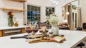 Une cuisine bien éclairée, dotée d’un plan de travail en marbre, de verres à vin, d’une planche à fromages et d’un vase rempli de fleurs.