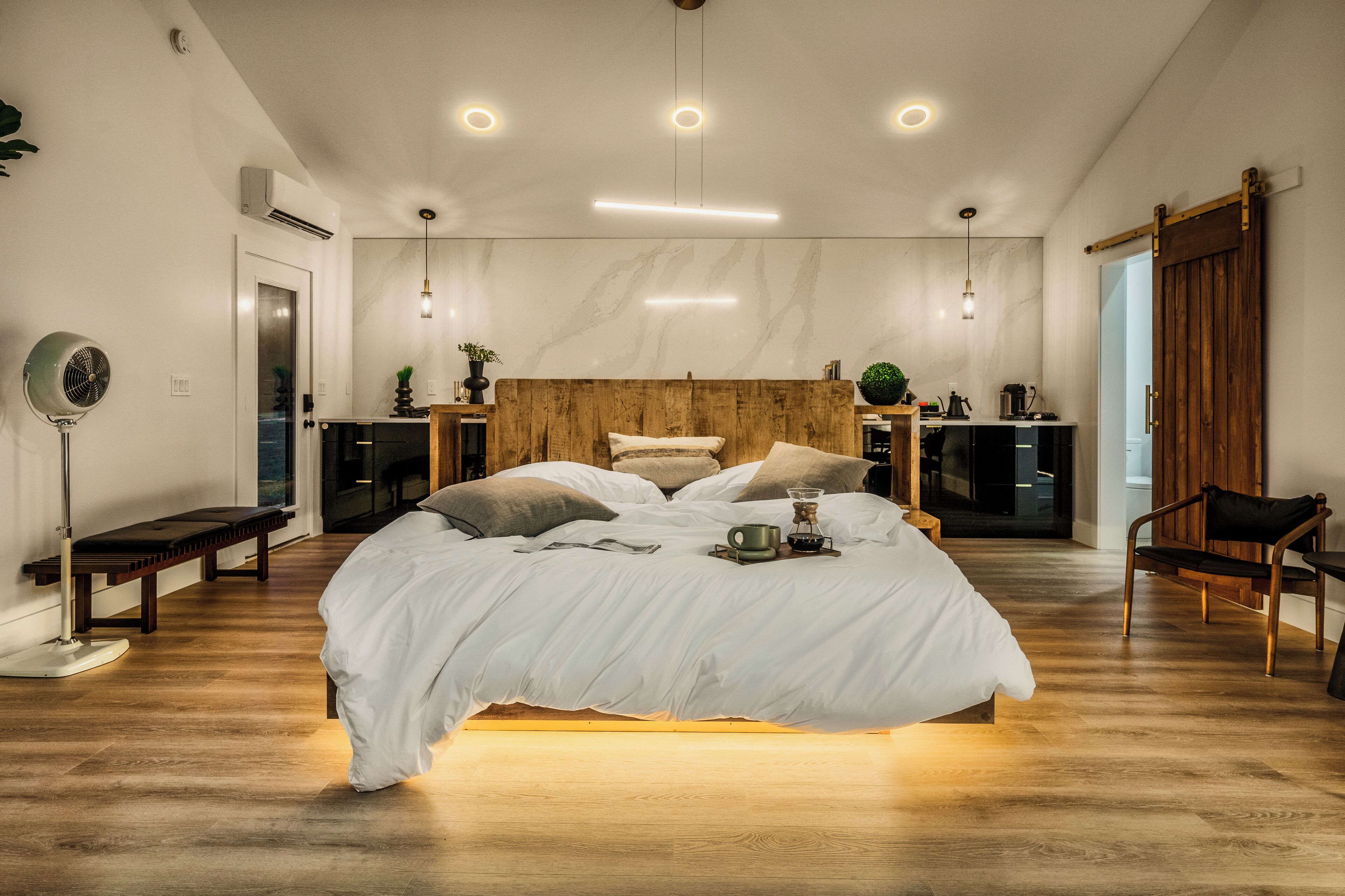 Um quarto moderno com cabeceira de madeira, uma cama grande, mesas de cabeceira, uma luminária de chão e uma porta de correr.