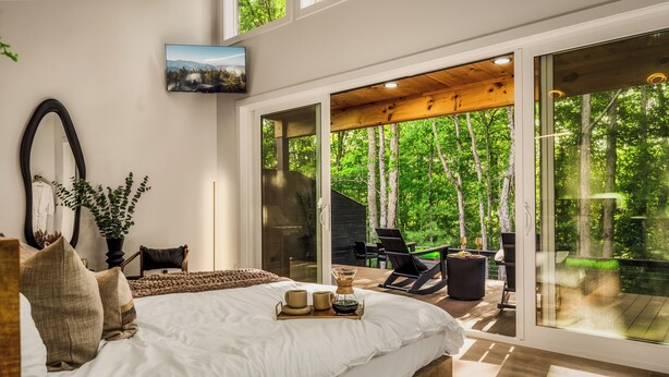 A bedroom with a large bed, a mirror, and a view of a forest through glass doors. - The 110 Copse (Wartburg)
