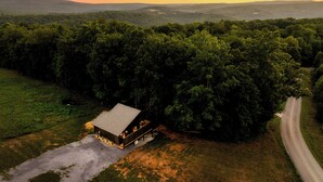 A cabin with a large porch, surrounded by dense forest, with a road curving to the right. - The 110 Copse (Wartburg)
