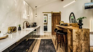A modern kitchen with a long countertop, a wooden bar counter, and a dining area with stools. - The 110 Copse (Wartburg)
