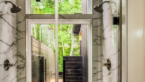 A modern bathroom with a glass-enclosed shower, marble walls, and a view of a wooden deck and greenery outside. - The 110 Copse (Wartburg)