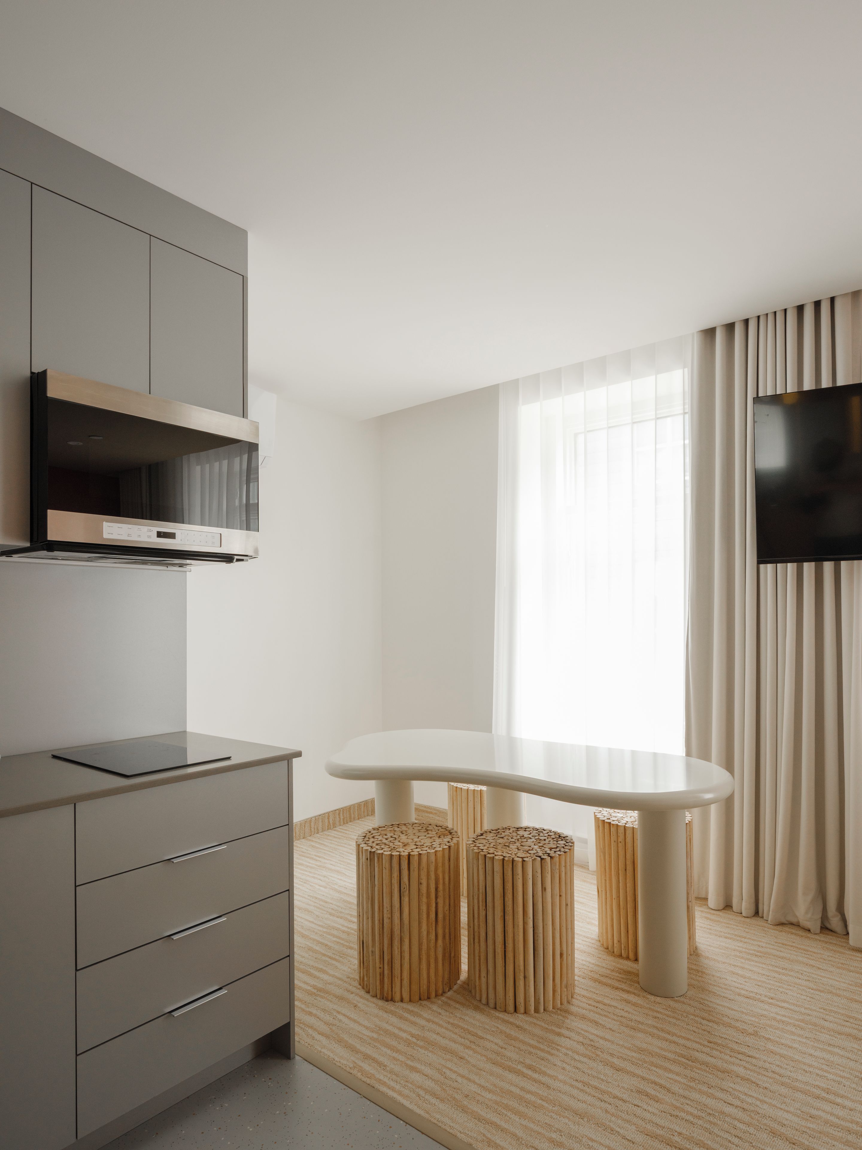 A modern kitchen with a built-in microwave, a flat-screen TV mounted on the wall, and a dining area with a white table and two stools.