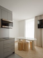 Una cocina moderna con microondas integrado, televisor de pantalla plana en la pared y zona de comedor con mesa blanca y dos taburetes.