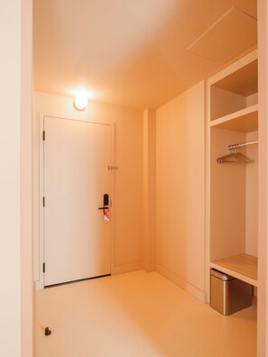 A narrow hallway with a closed door, a trash bin, and a closet with a hanging rod.