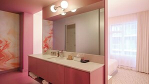 A modern bathroom with a pink vanity, a large mirror, and a window with curtains. - Rose Hôtel Invisible (Québec)