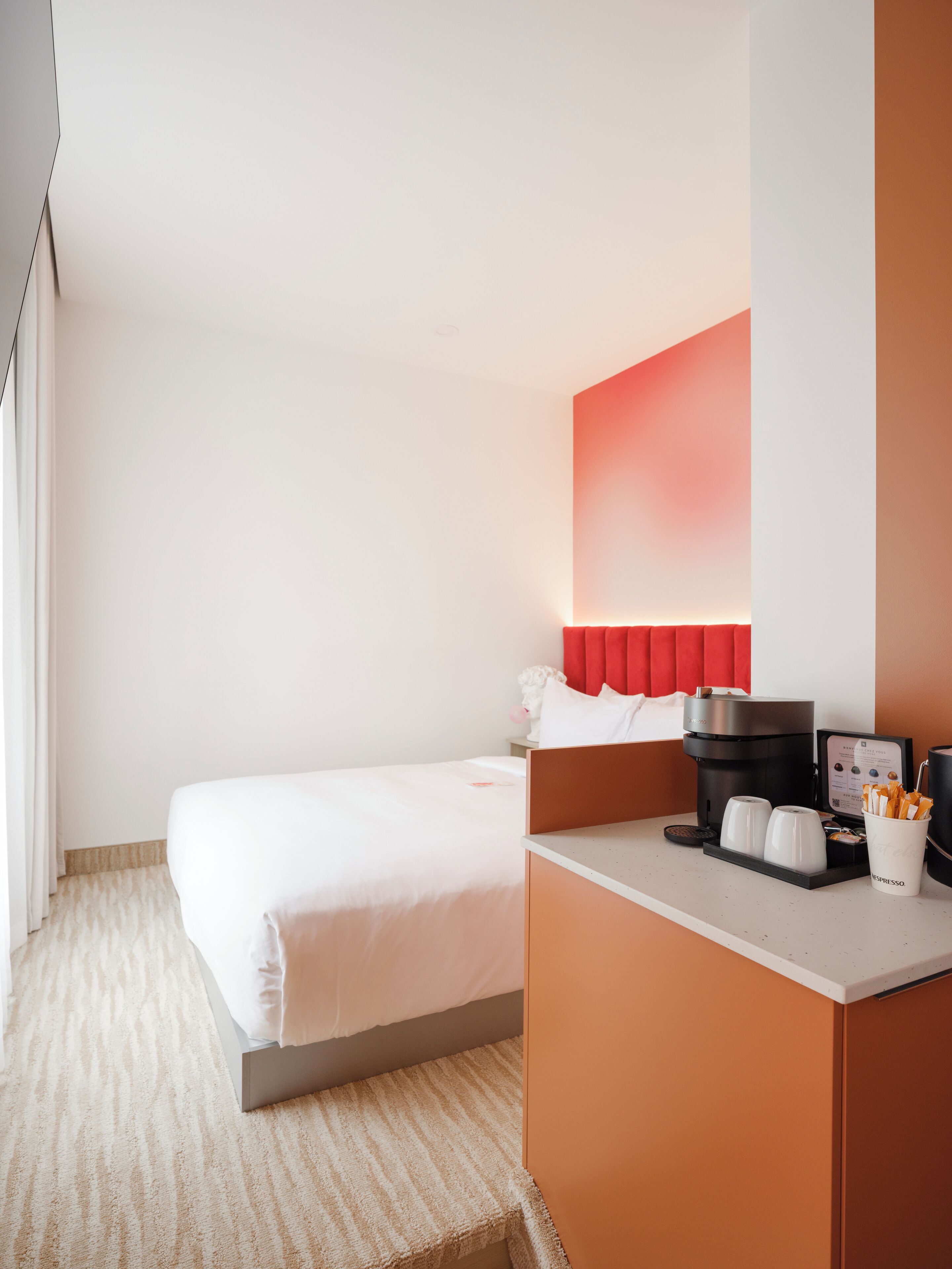 Quarto de hotel com cama, cafeteira e uma chávena de café sobre o balcão.