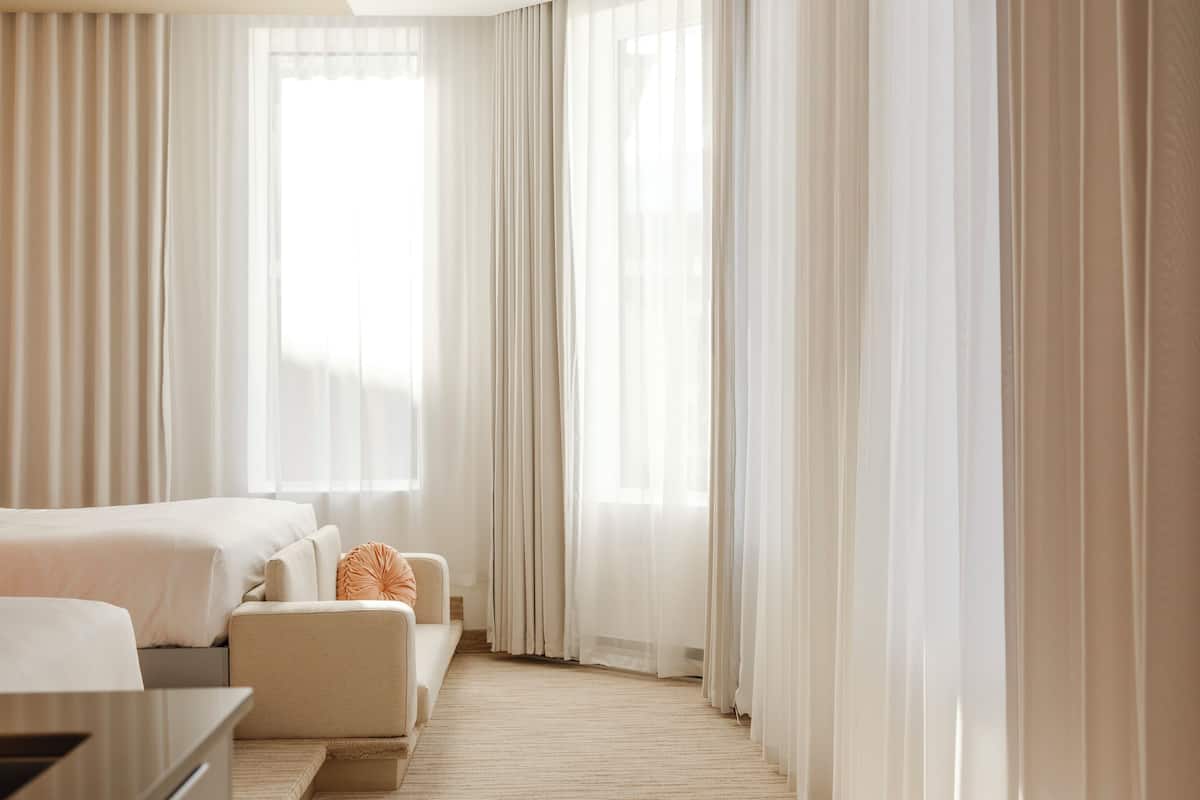 A modern hotel room with a large window, a sofa, a chair, and a desk.