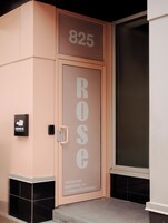 Entrada de hotel con el número '825' sobre la puerta, el nombre 'ROSE' en la puerta y un letrero de 'ROSEHOTEL.CA' con un número de teléfono y un identificador de Instagram.