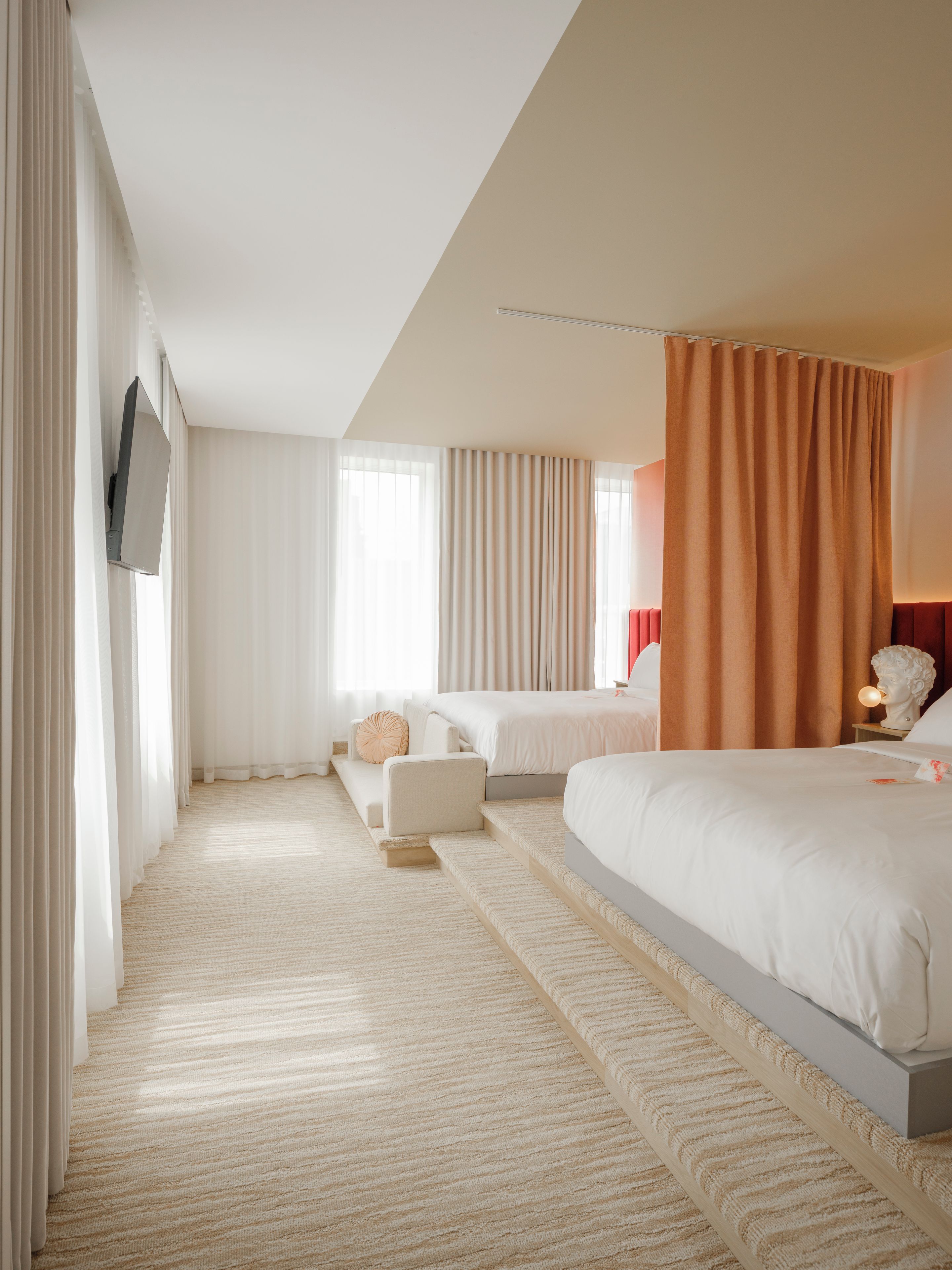 A hotel room with a large bed, a smaller bed, a sofa, and a television mounted on the wall.