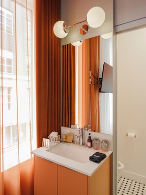 A modern bathroom with a large mirror, a white sink, and a shower area.