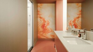 A modern bathroom with a large mirror, a white sink, and a shower area. - Rose Hôtel Invisible (Québec)