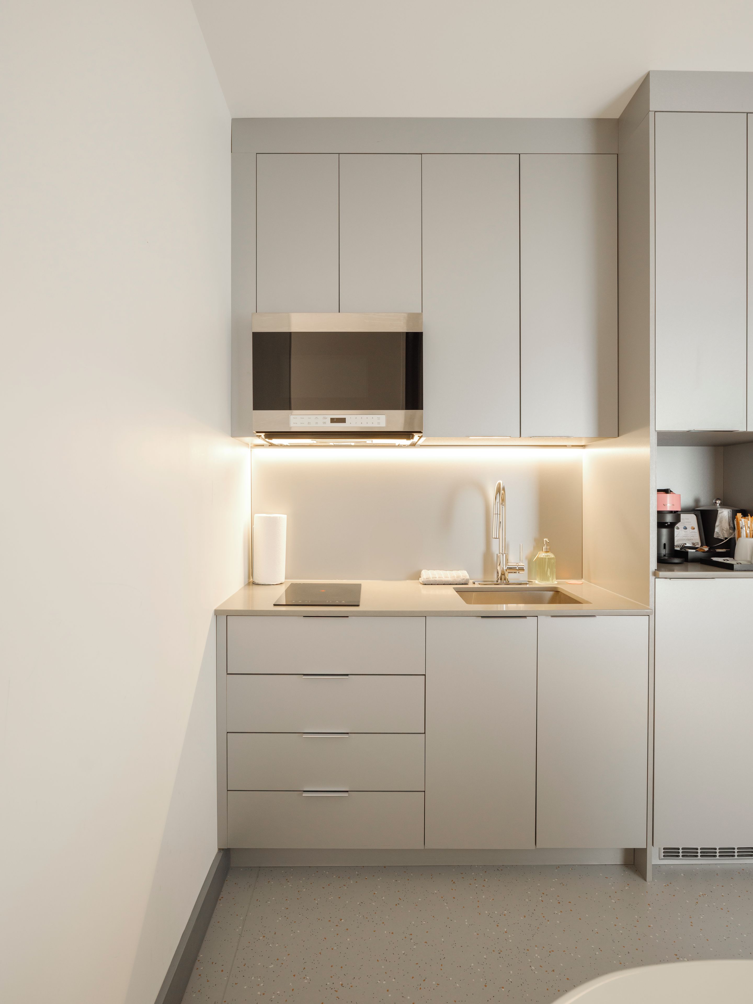 Eine moderne Küche mit Einbau-Mikrowelle, Spüle und einer Arbeitsfläche mit Wasserkocher und Flasche.