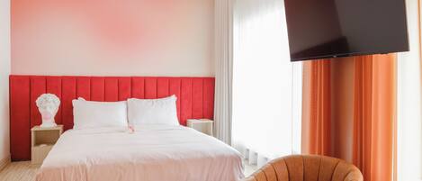 Ein modernes Hotelzimmer mit einem Bett, einem Flachbildfernseher, einer roten Akzentwand und einem braunen Sessel.