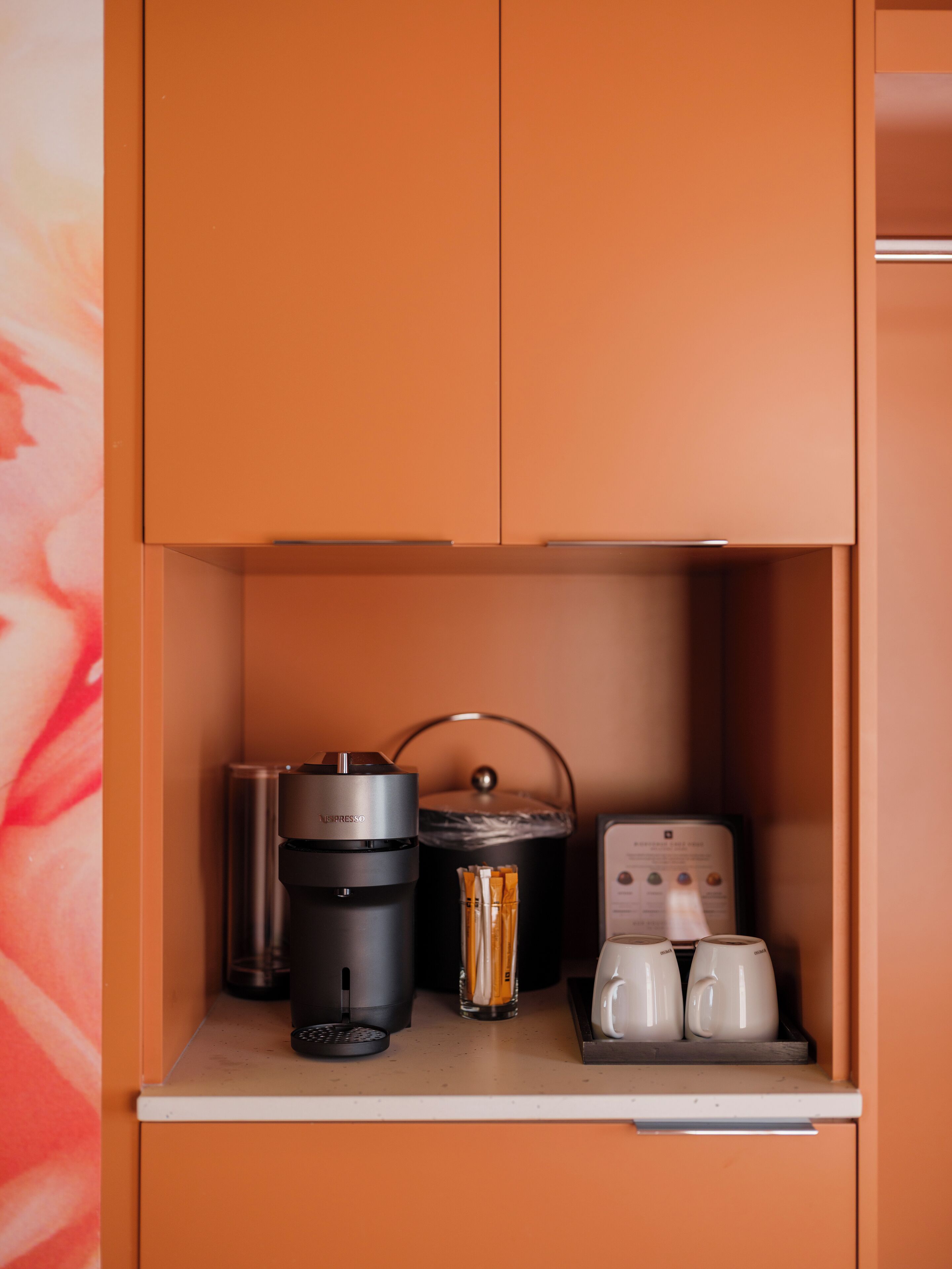 A kitchenette with a coffee maker, a kettle, and two mugs on the counter.