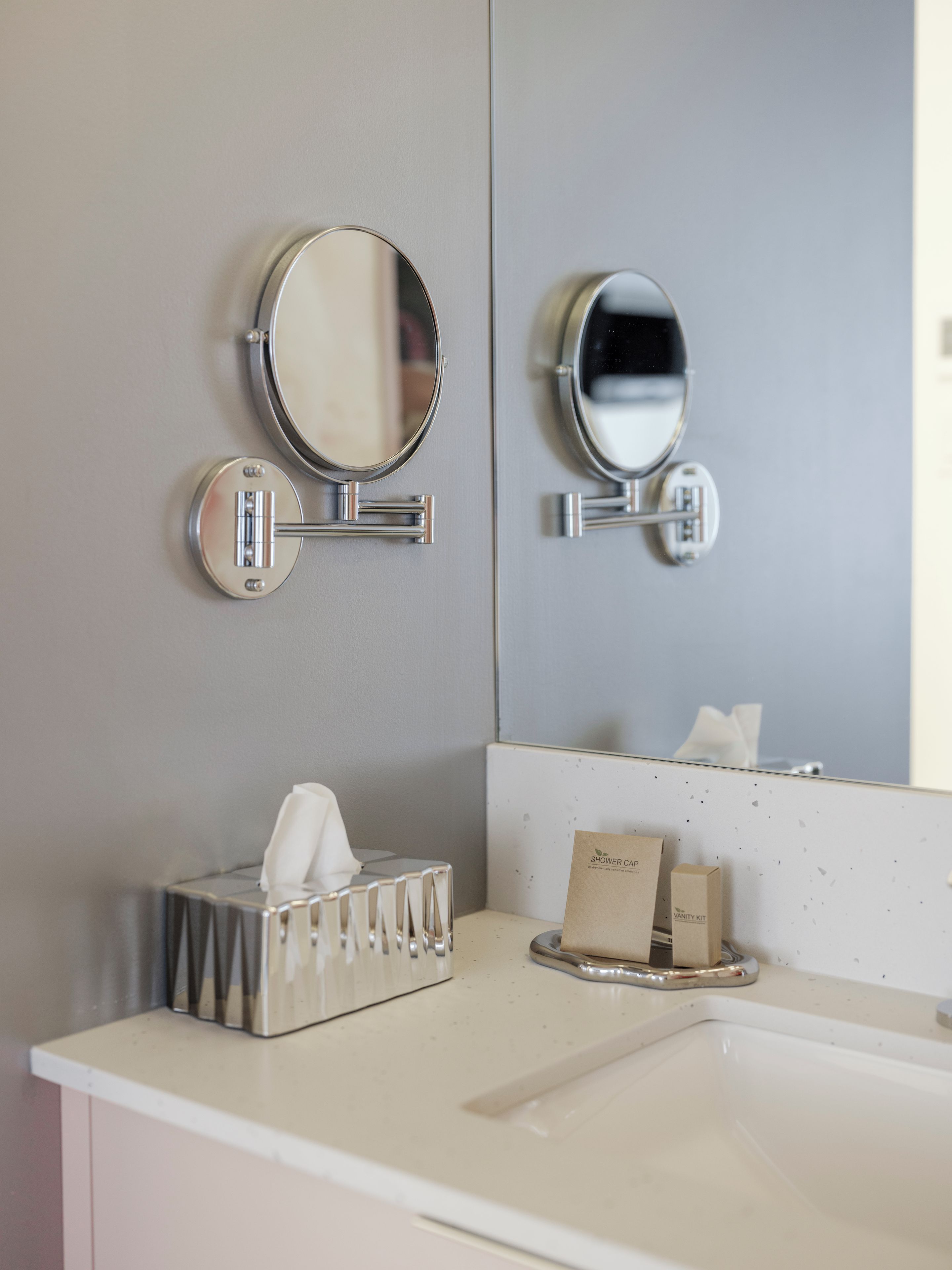 A bathroom with two wall-mounted mirrors, a tissue dispenser, and a vanity kit on the counter.