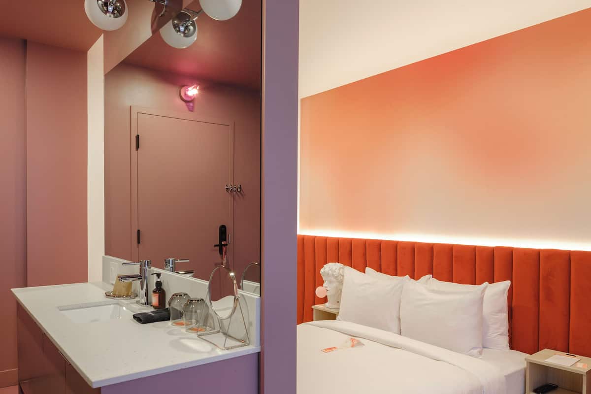 A modern hotel room with a large bed, a separate bathroom with a vanity, and a unique ceiling light fixture.