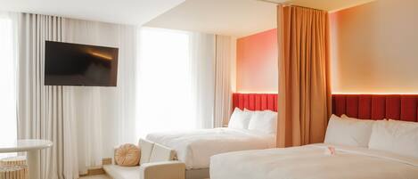 Hotelkamer met een groot bed, een kleiner bed, een flatscreen televisie aan de muur, een zithoek met een tafel, en een raam met gordijnen.
