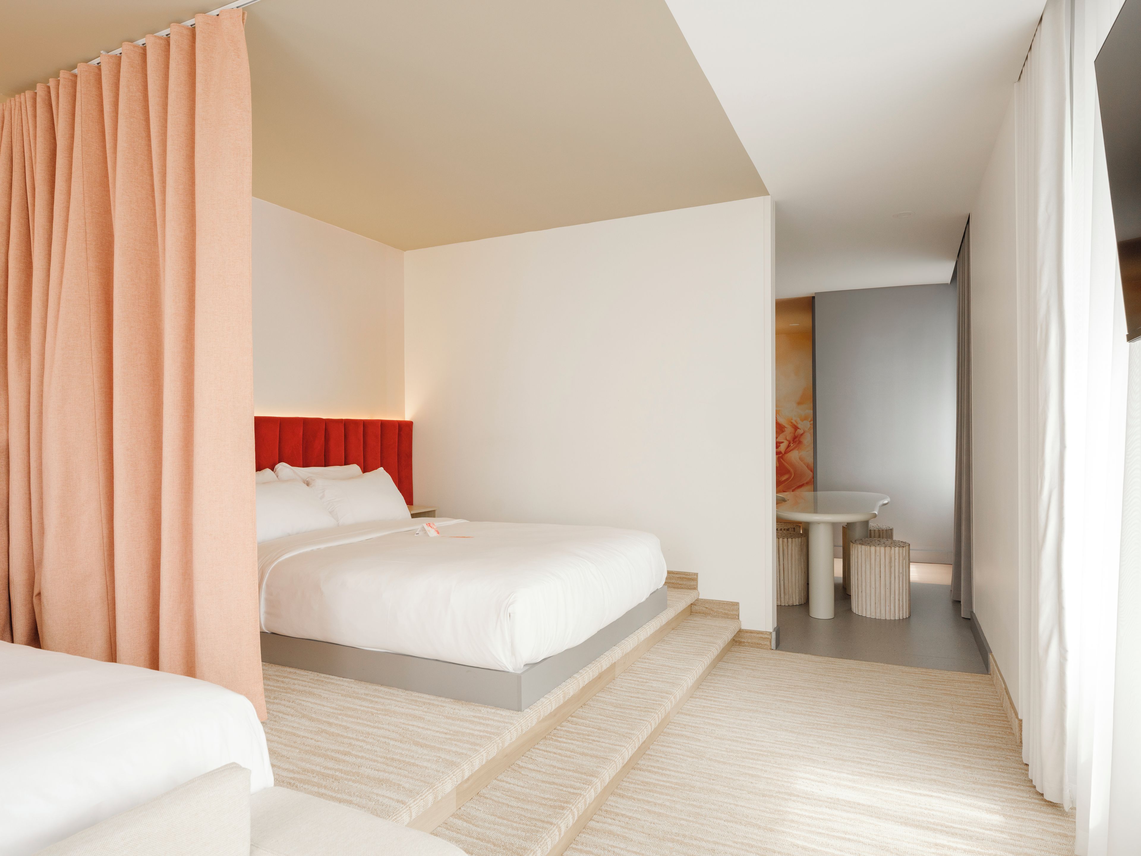 Une chambre d’hôtel moderne avec un grand lit, une petite table et une salle de bain visible à travers une porte ouverte.