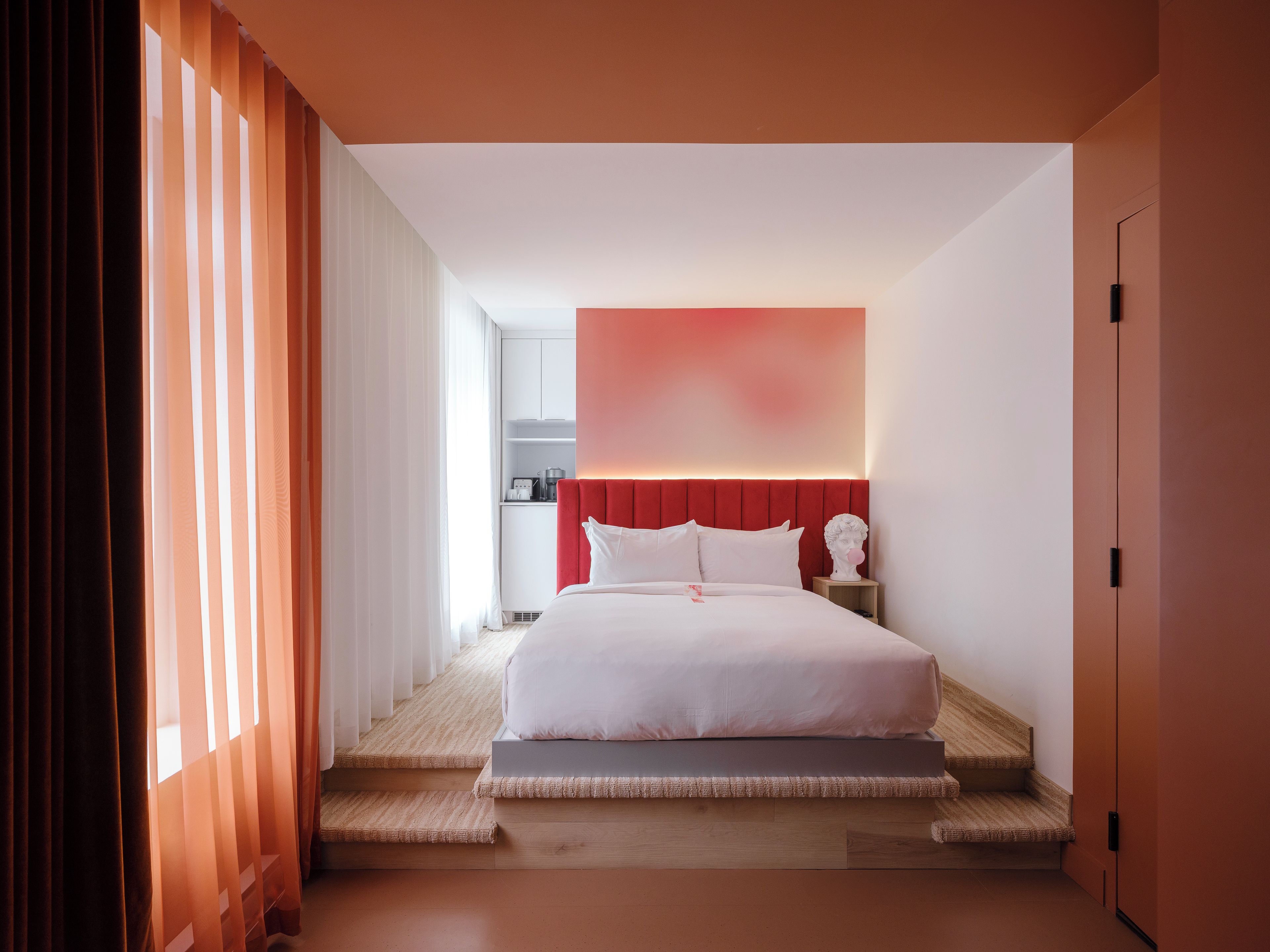 Una habitación de hotel moderna con una cama grande, una pared de acento roja y vistas al área de la cocina.