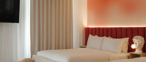 A hotel room with a large bed, a smaller sofa, a flat-screen TV mounted on the wall, and a decorative bust on the nightstand.
