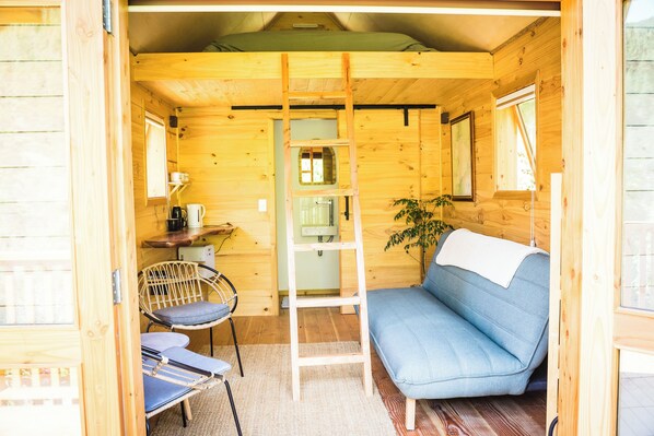 A cozy cabin interior with a blue sofa, a ladder, a chair, and a small table with a kettle.