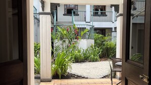 An open doorway to a courtyard with a tiled floor, a small table with chairs, and a variety of plants. - The Victorian Hotel CR (San José)