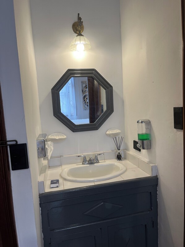 A bathroom with a white sink, a black vanity, a mirror, and a light fixture above the mirror.