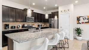 A modern kitchen with dark cabinets, granite countertops, stainless steel appliances, and pendant lighting. - Spacious 5-bedroom townhome in gated community. Minutes from Disney! Sleeps 10 (Davenport)