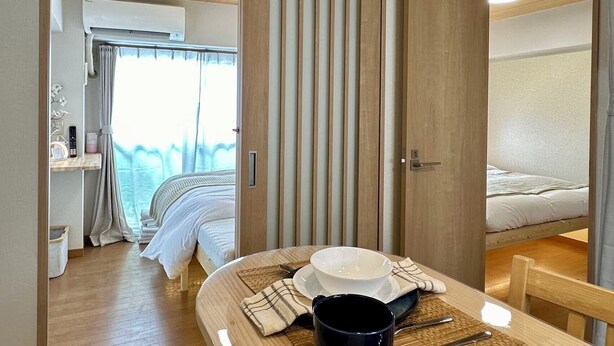 Ein modernes, kompaktes Zimmer mit einem Etagenbett, einem kleinen Esstisch, einer Schüssel und Besteck sowie einem Fenster mit Vorhängen.