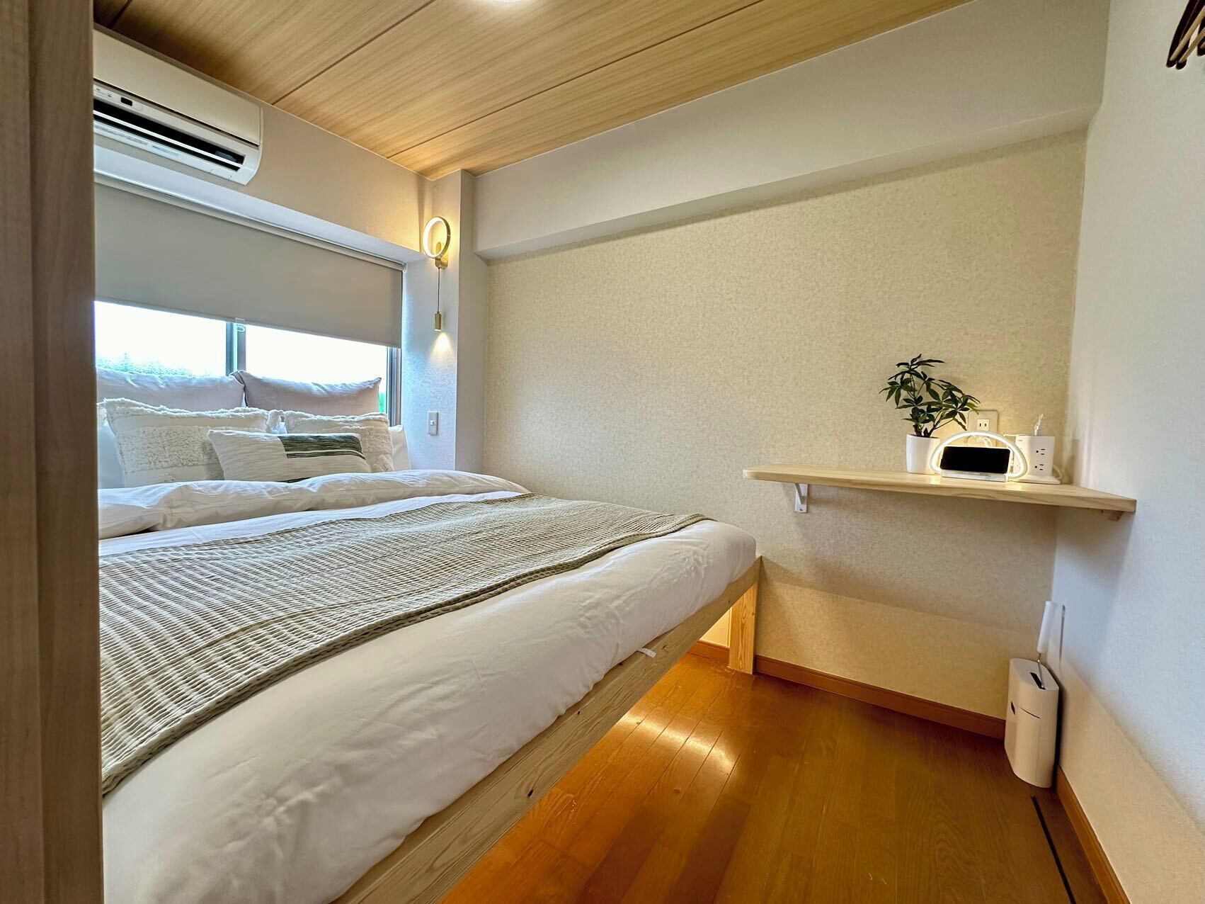 A bedroom with a bed, bedside table, and a wall-mounted shelf with a plant and electronic devices.