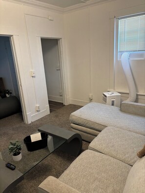 Ein kompakter Wohnraum mit einer Couch, einem kleinen Tisch und einem Fenster mit Jalousien.