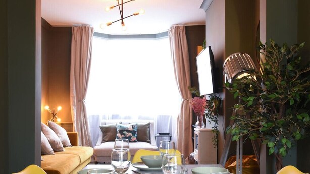 Un comedor con una mesa dispuesta para cuatro, un sofá al fondo y una planta a la derecha.